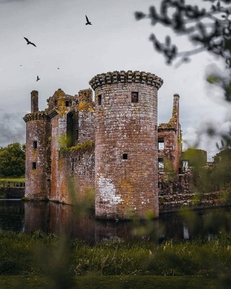 Birds circle above Caerlaverock Castle's moated ruins and round tower