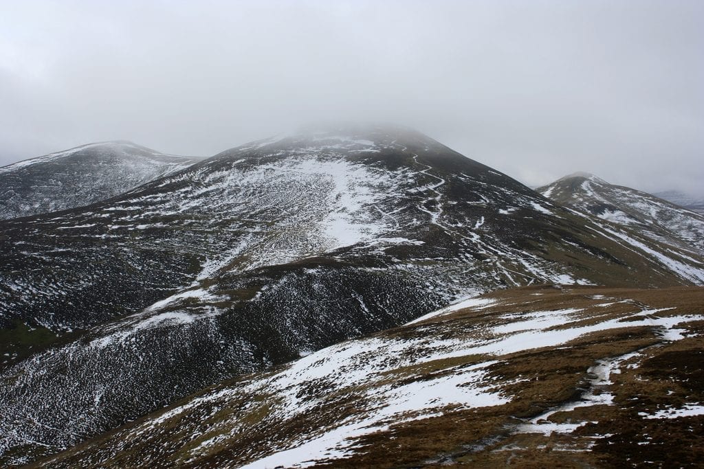 Snow-streaked mountain ridge disappearing into low grey cloud