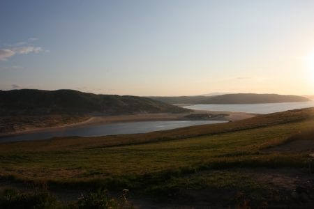 Sun setting over a river estuary winding between grassy hills