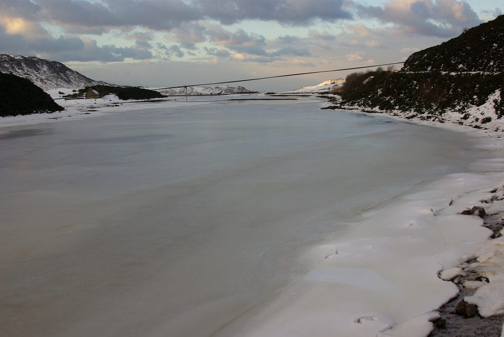 Frozen loch surrounded by snow-dusted hills under a cloudy sky