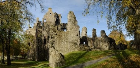 Ruined stone castle towers rise above autumn trees and a grassy path