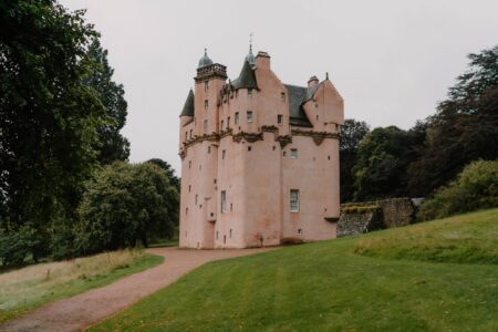 Pink-hued Craigievar Castle with turrets rising above trees and lawns