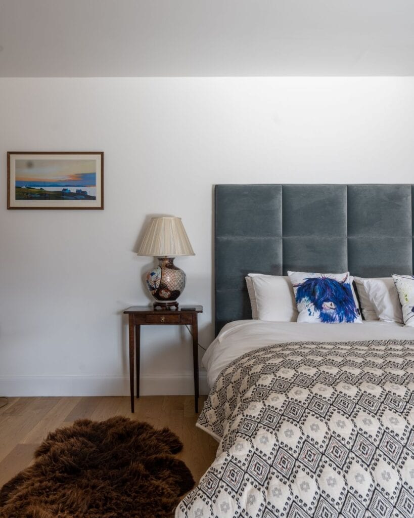 Bedroom with grey upholstered headboard, patterned throw and Highland cow cushion