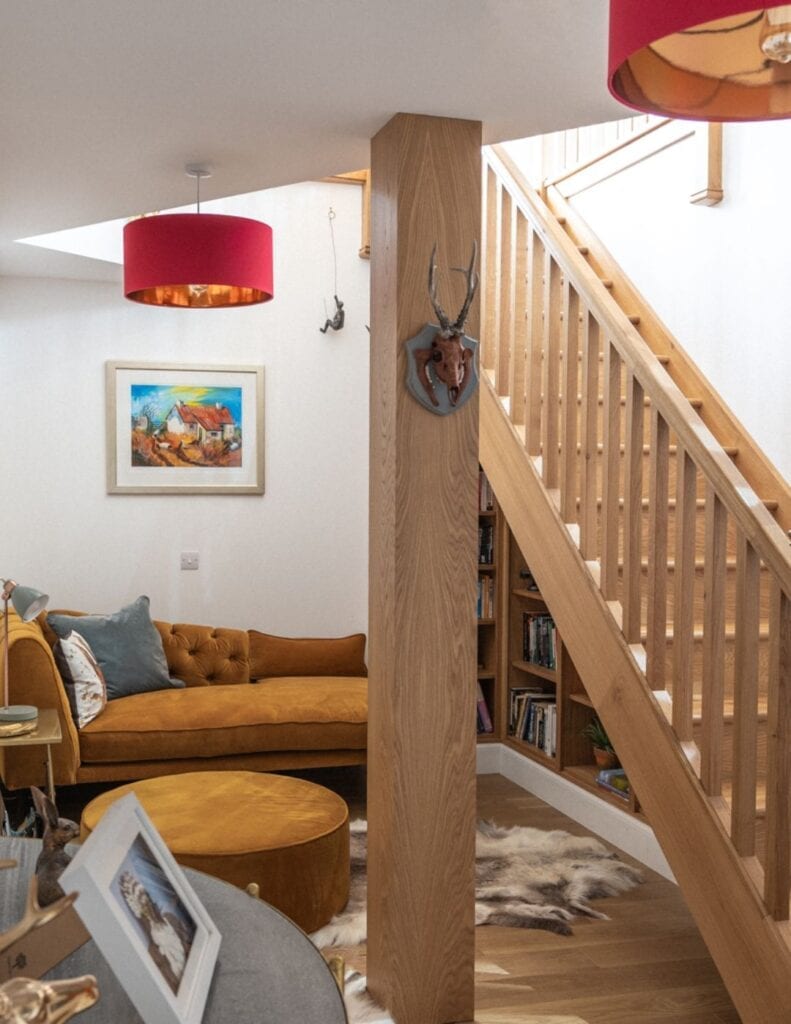 Wooden staircase and stag ornament beside a mustard velvet sofa