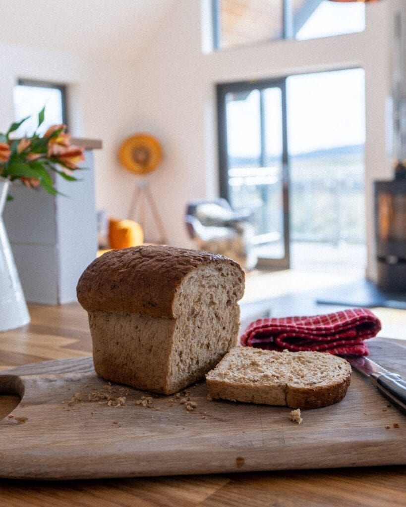 Sliced brown loaf on a wooden board beside a woodburning stove
