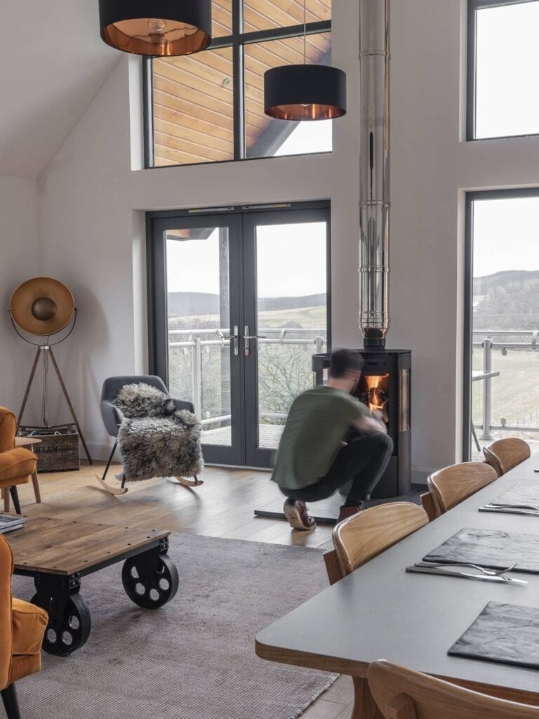 A man crouches by a wood burning stove in a hillside living room
