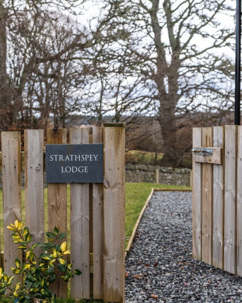 Wooden gate marked "Strathspey Lodge" opens onto a gravel path