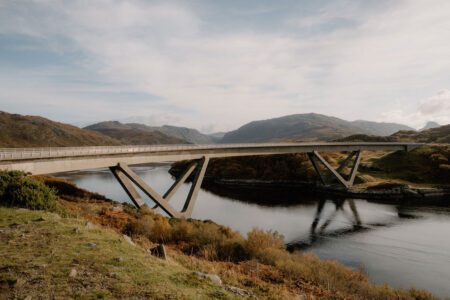 Concrete road bridge with V-shaped supports crossing a loch amid hills