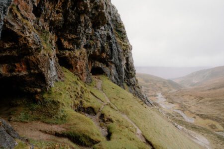 Rocky overhang above a grassy slope overlooking a misty glen