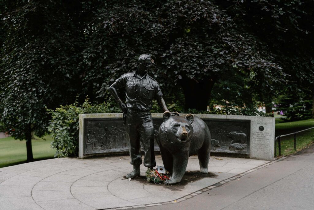 Bronze statue of a soldier standing beside a bear, with flowers laid at its base