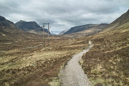 The rough path of the West Highland Way climbing through a wide, bare glen towards the hills.