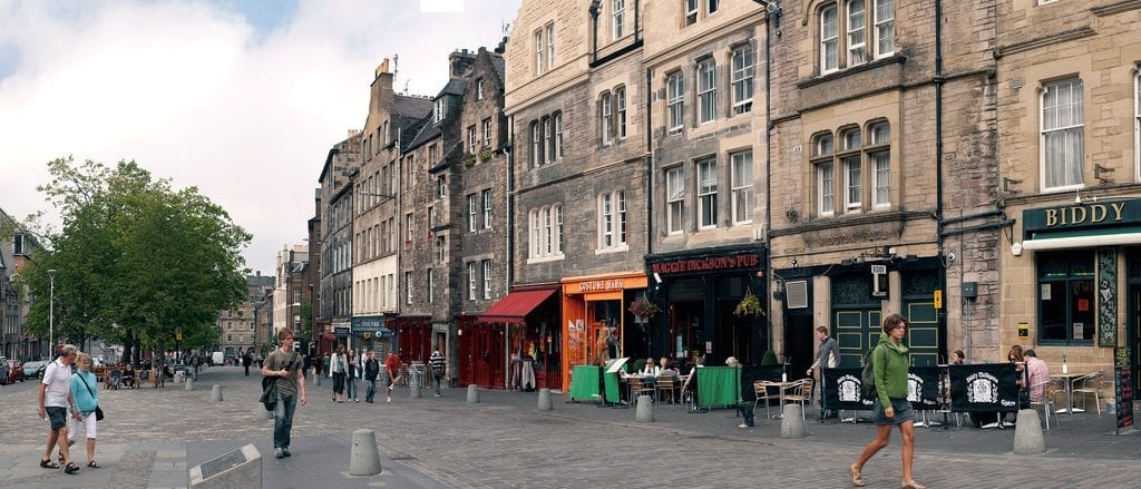 Pedestrians walk along the Grassmarket, with Biddy's pub sign visible on the right