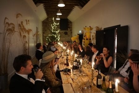 Guests raise wine glasses at a long candlelit table in a stone barn