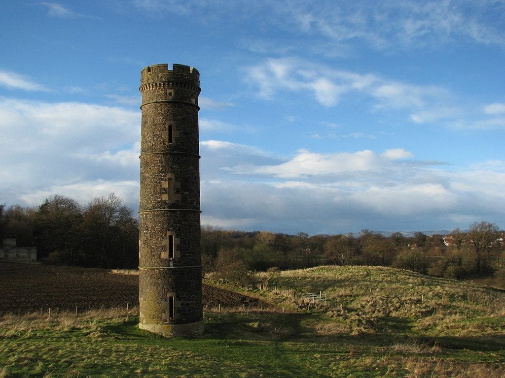 Round stone tower with battlements standing above open farmland