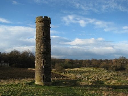 Round stone tower with battlements standing above open farmland
