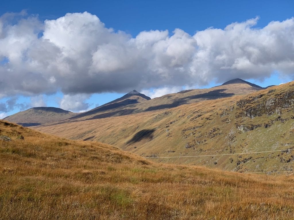 Ben Oss and its neighbours above golden grass under big clouds.