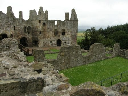 Ruined stone walls and towers surround a grass courtyard at Dunbar Castle