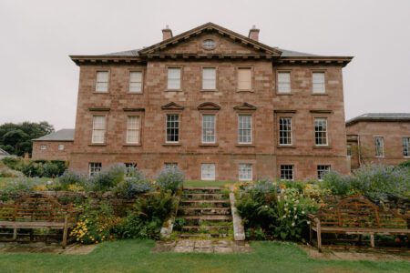 Sandstone mansion with pediment roof, stone steps leading through terraced garden borders