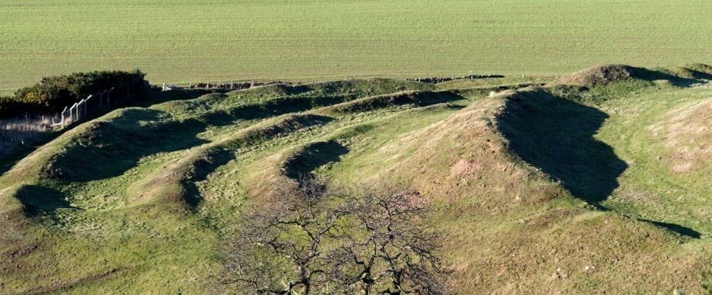 Grass-covered earthwork ramparts curve across a hillside, casting long shadows