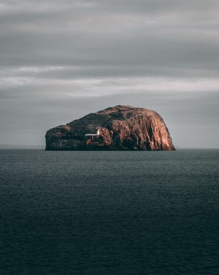 Bass Rock rises from grey sea, its white lighthouse visible on the slope