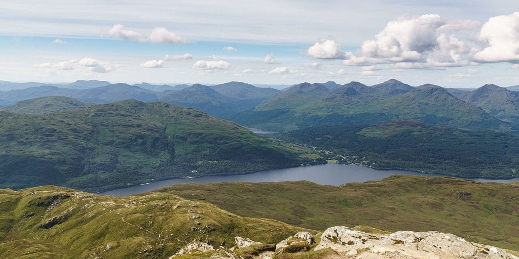 Loch Lomond winds between mountain ranges, seen from a high grassy summit