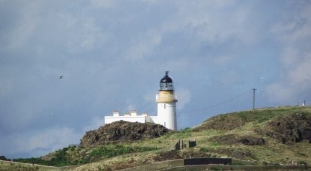 White lighthouse with black lantern room atop a rocky, grassy headland