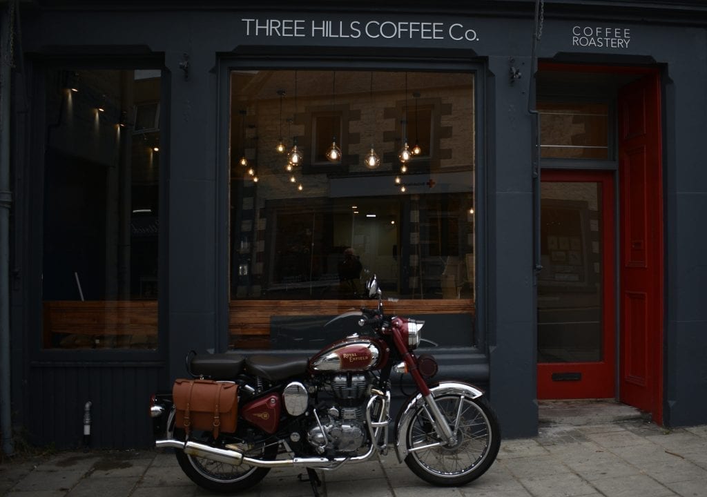 Motorcycle parked outside Three Hills Coffee Co, with a red Coffee Roastery door