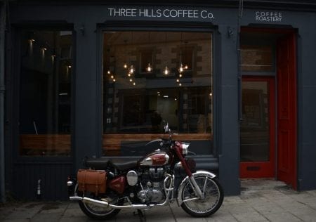 Motorcycle parked outside Three Hills Coffee Co, with a red Coffee Roastery door