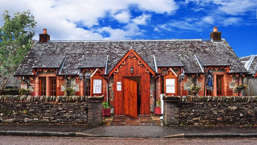 The Village Rest, a whitewashed cottage with a red timber porch in Luss.