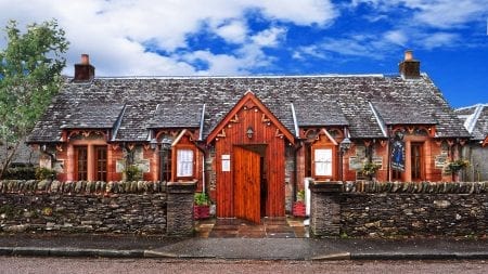 The Village Rest, a whitewashed cottage with a red timber porch in Luss.
