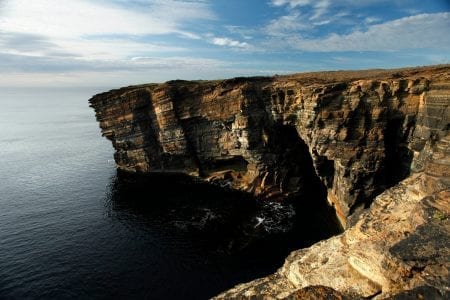 The layered sandstone cliffs of Yesnaby dropping into a calm dark sea, lit by low sun.