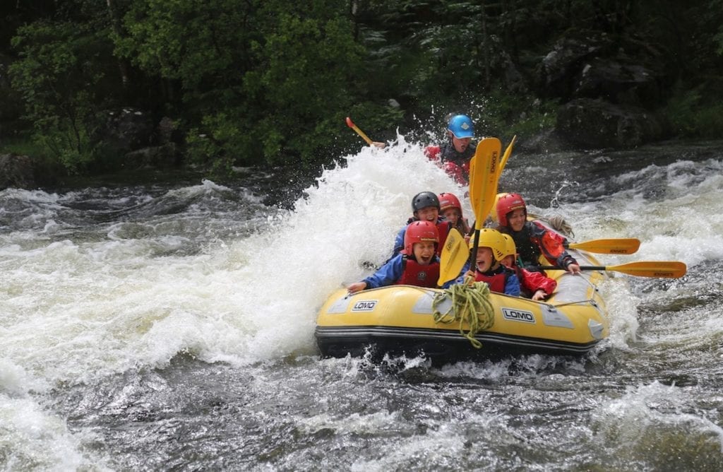 Rafters in helmets paddle through white water rapids on a yellow inflatable raft