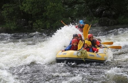 Rafters in helmets paddle through white water rapids on a yellow inflatable raft