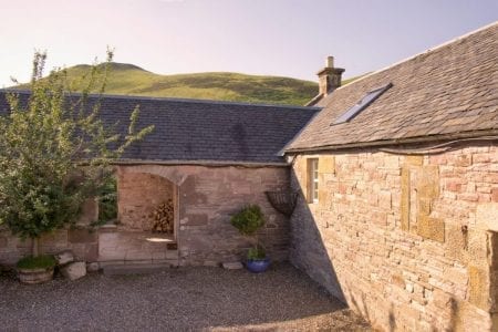 Stone cottage courtyard with slate roof, chimney and rolling green hills behind