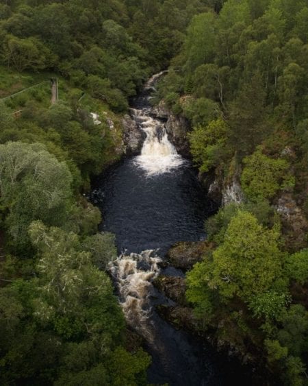 Waterfall cascading through a wooded gorge lined with dense trees