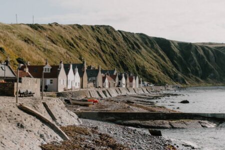Row of white cottages beneath a grassy cliff along a pebble shoreline