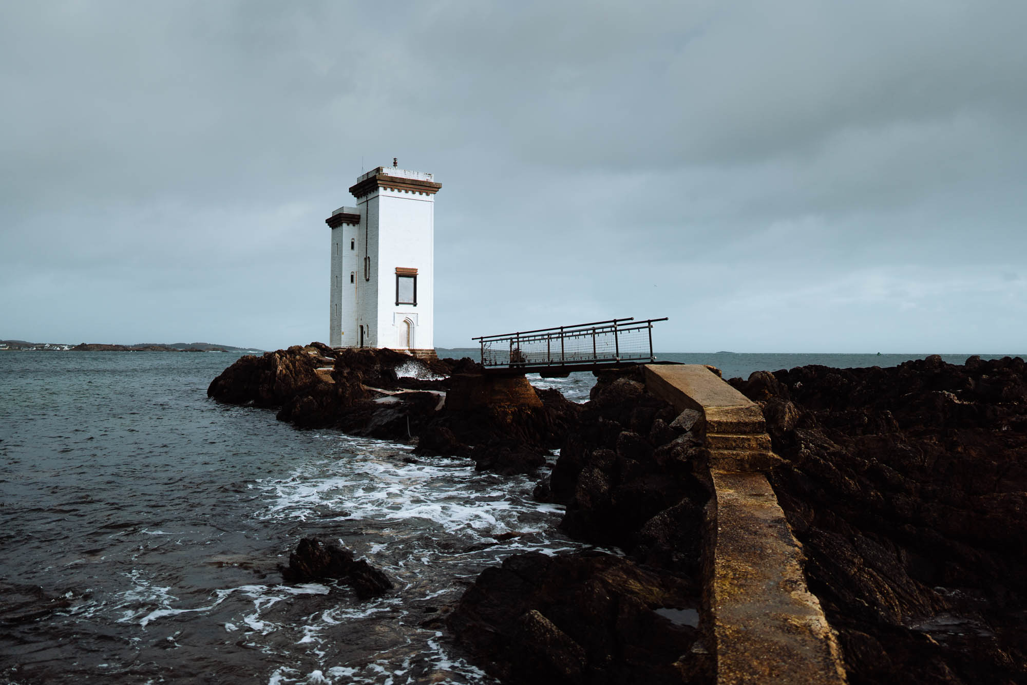 Carraig Fhada lighthouse on its rocky point under a dark sky.
