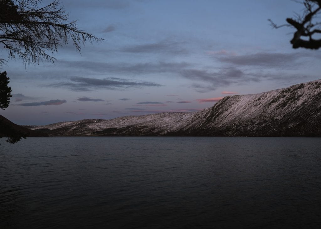 Snow-dusted hills reflect fading light over a still loch at dusk
