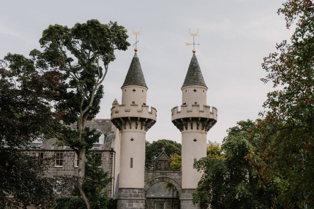 Twin turreted gatehouse towers with crescent moon weathervanes among trees