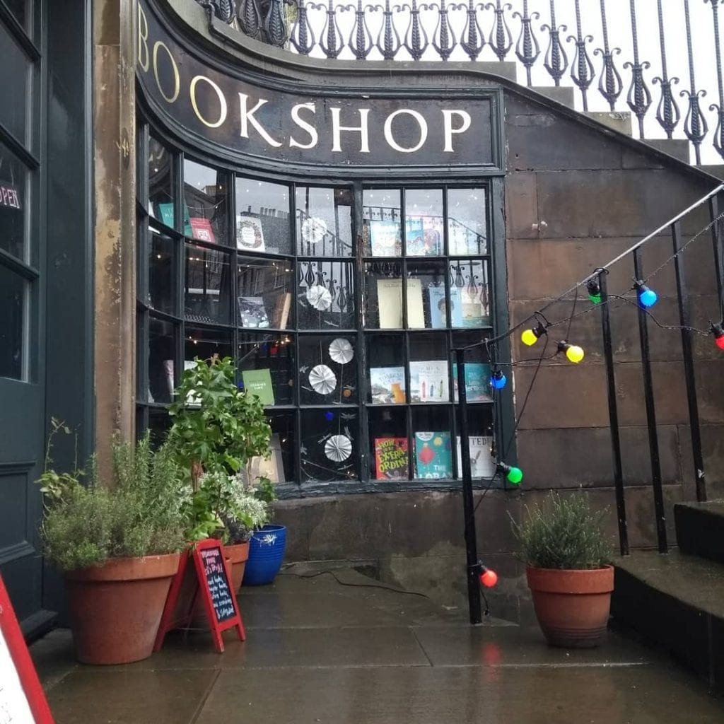 Bay window of a bookshop, potted plants and coloured fairy lights outside