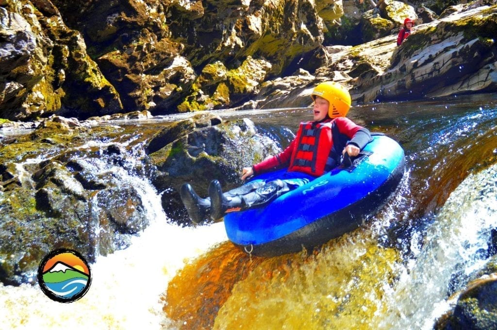 Child in helmet and life jacket rides a rubber tube over rapids