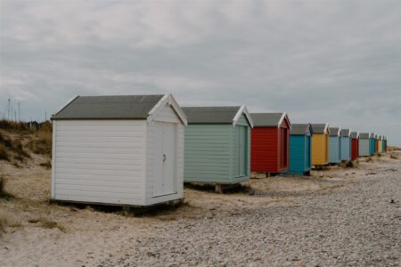 Row of colourful wooden beach huts on a pebbled shore under grey skies