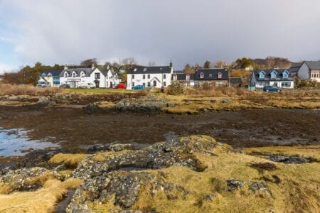 White houses along the shoreline at low tide, seaweed-covered rocks in foreground