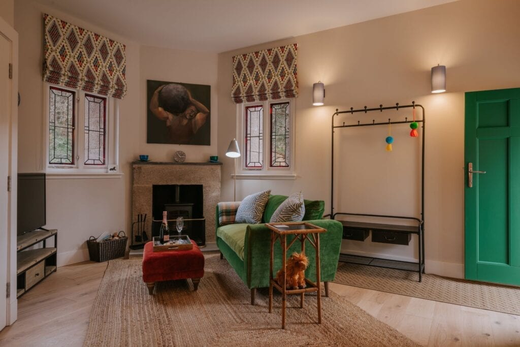 A small dog rests against a copper-legged side table beside a green velvet corner sofa, a coat rack strung with balloons and a framed portrait above the fireplace.