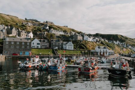 Fishing boats moored in Gardenstown harbour beneath white houses on the hillside