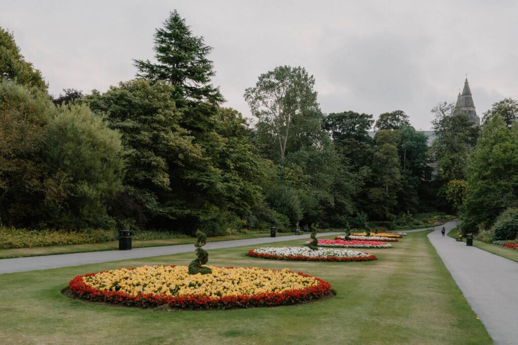 Circular flowerbeds line a park path, a spire visible through the trees