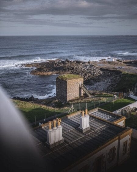Stone tower on a rocky headland, seen beyond rooftop chimneys