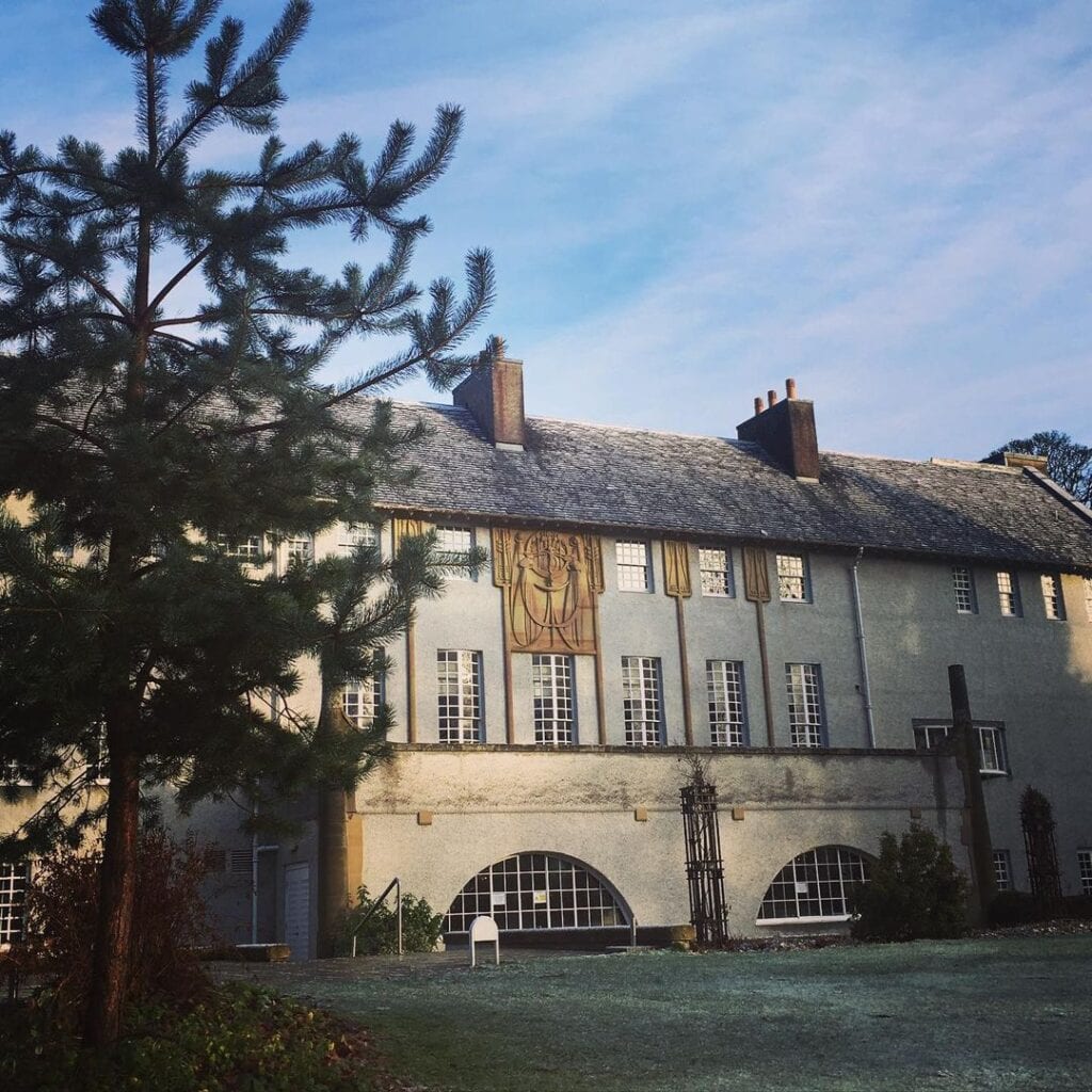 House for an Art Lover behind a pine tree, its white front lit by low sun.