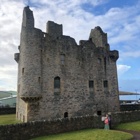 Scalloway Castle's roofless walls above its stone dyke, a visitor at the gate.
