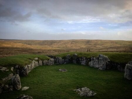 The heel-shaped stone walls of Stanydale Temple in the moorland under a cloudy sky.